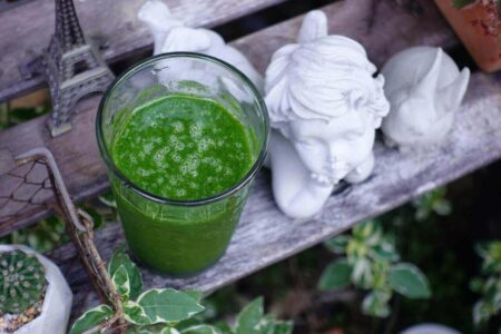 Close-Up Photograph of a Vegetable Smoothie Beside an Angel Sculpture