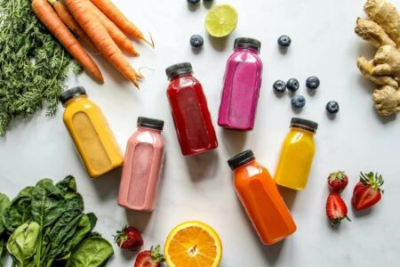 Colorful bottles of nutritious smoothies with carrots, ginger, leaves, and berries, representing balanced nutrition for vascular health.