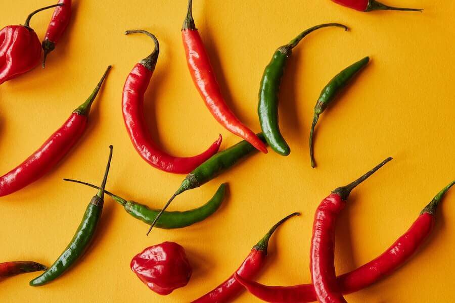 Assorted red and green peppers on a yellow background, representing the vibrant and flavorful world of spicy foods.
